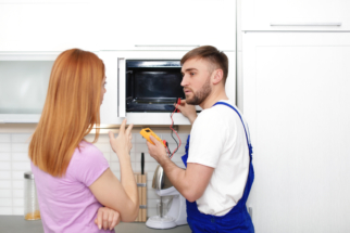 Housewife and repairman near microwave oven in kitchen